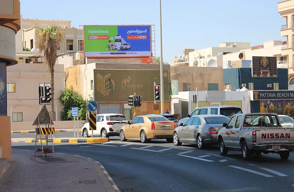 An OpenSooq billboard above a junction in Bahrain, with cars waiting at the lights