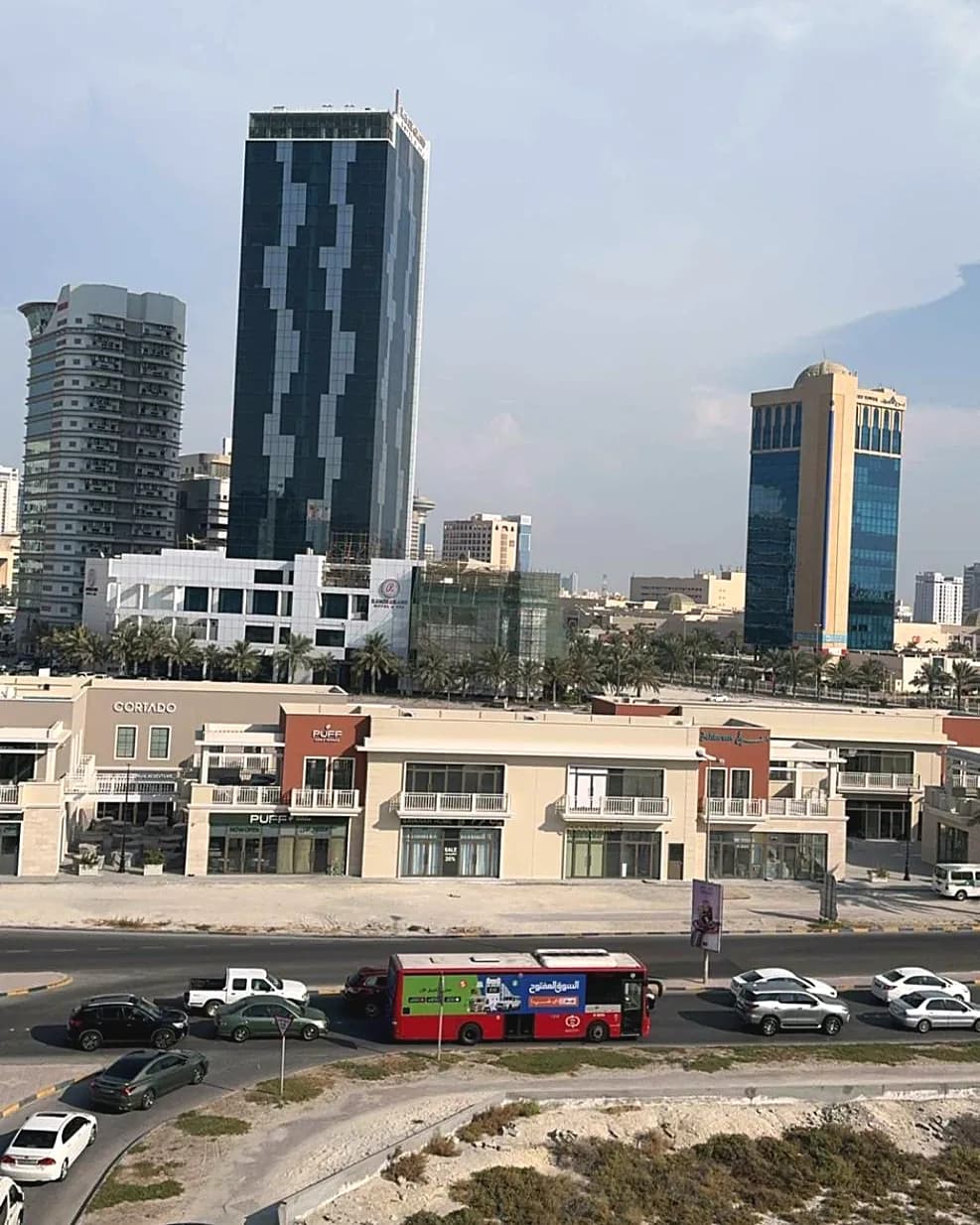 A wrapped OpenSooq bus on a road below the Manama skyline