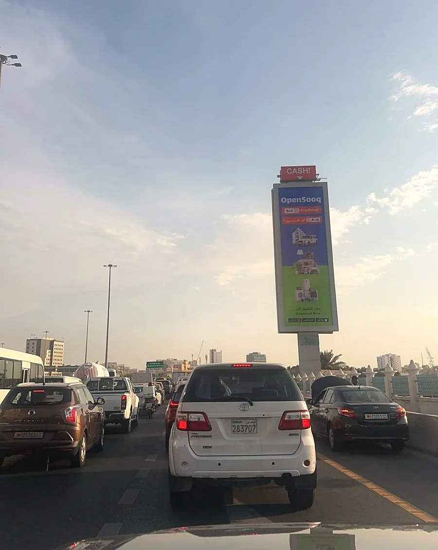 A tall roadside advertising panel carrying OpenSooq, seen from a car in traffic