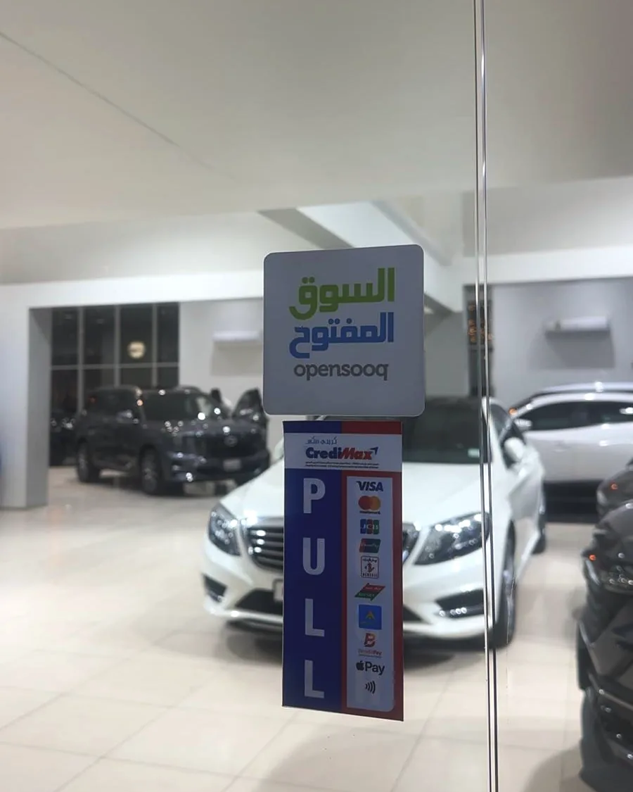 An OpenSooq decal on the glass entrance door of a car showroom